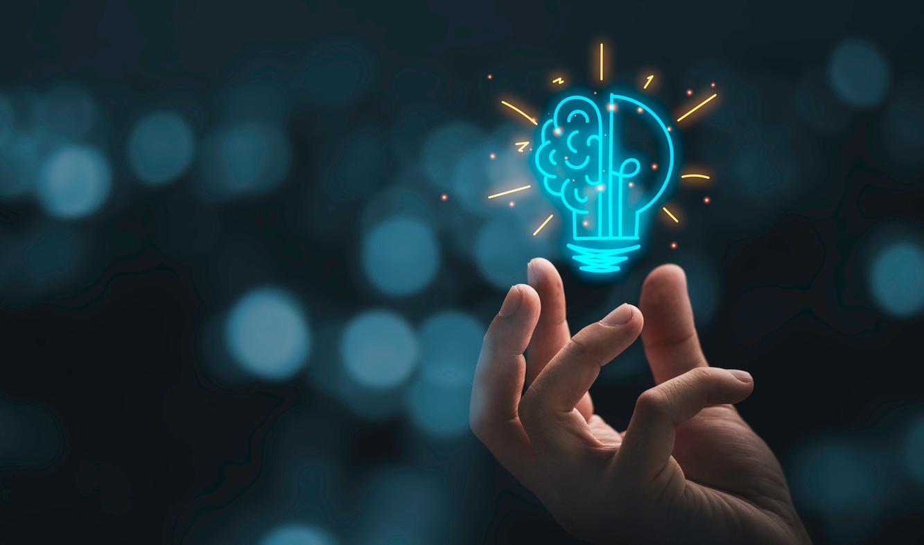 Hand holding a glowing lightbulb with a circuit-board brain